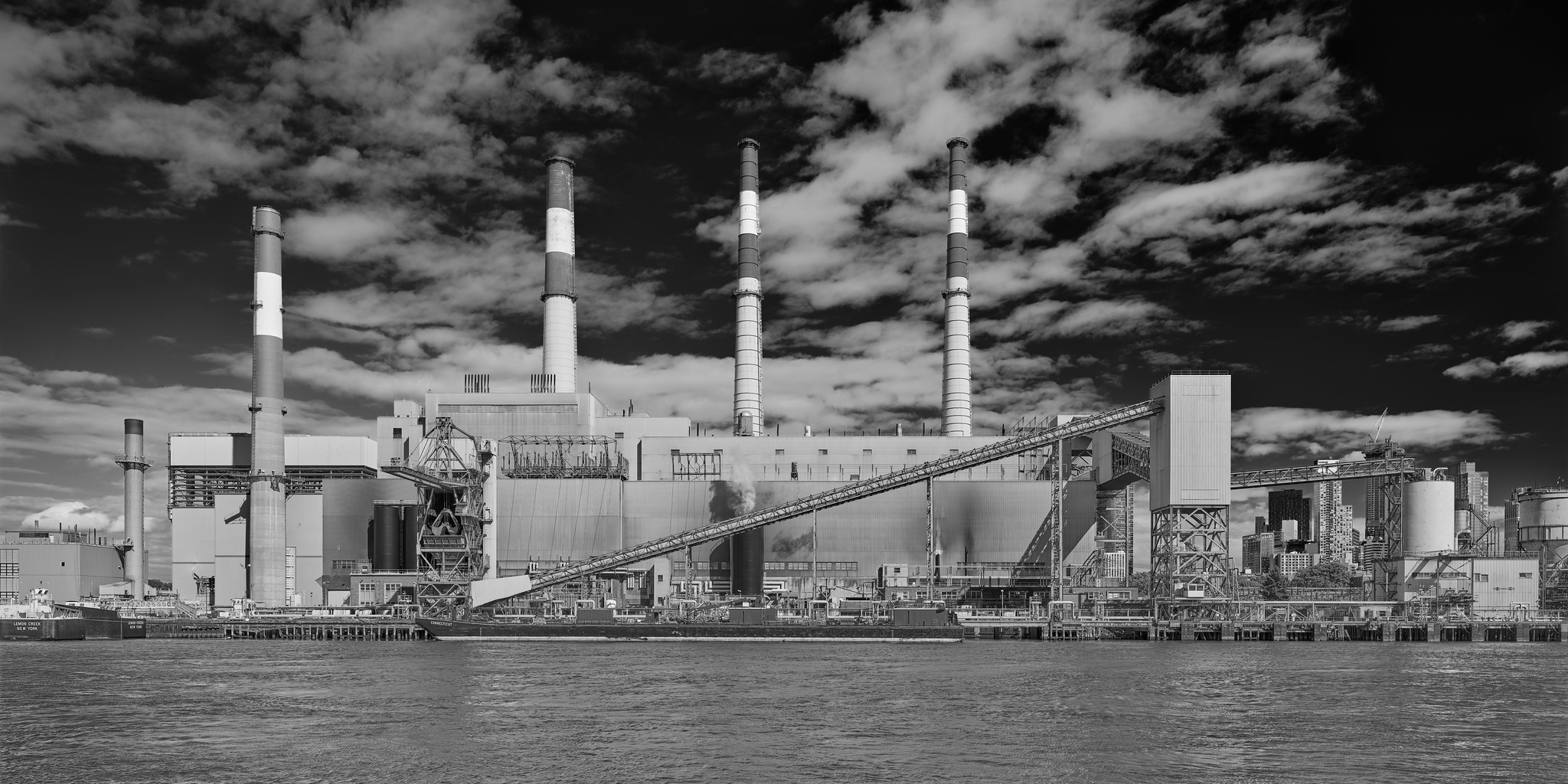 A large industrial building on a waterfront. Four large smokestacks, numerous pipes, elevators, and other apparatus are visible on the exterior.