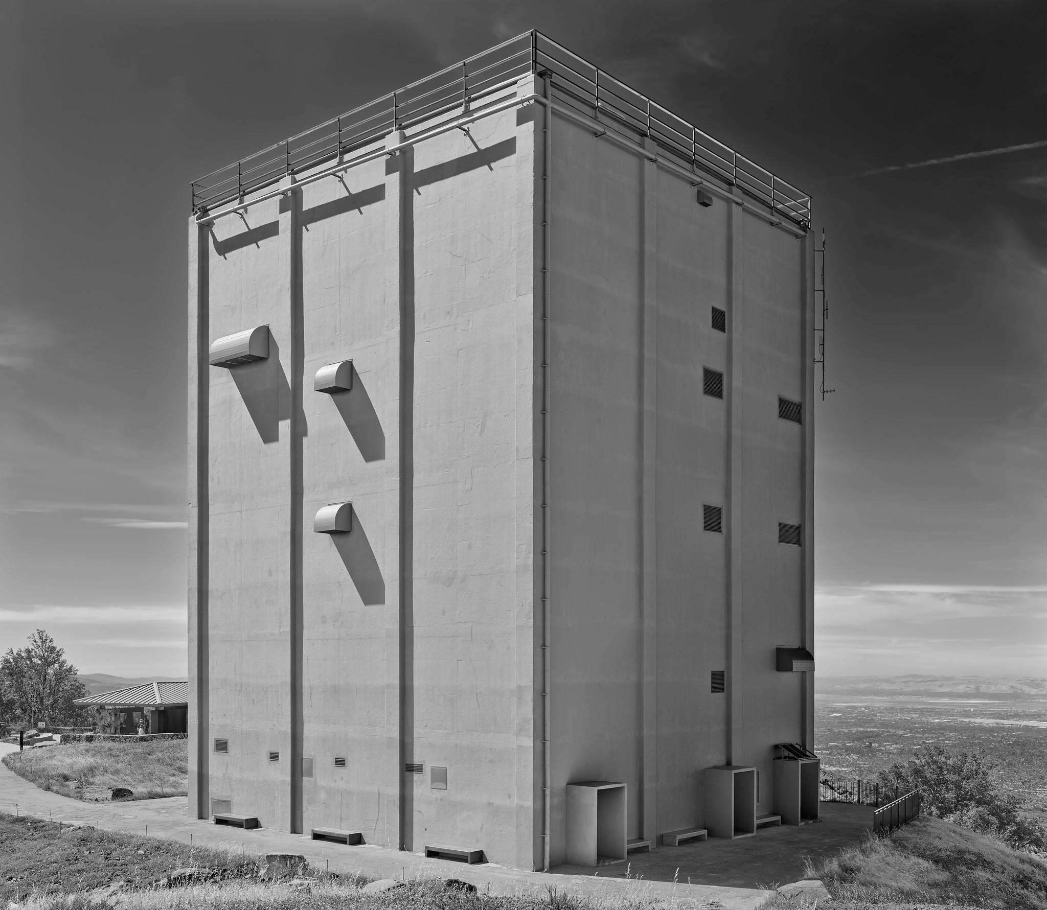 A large monolith-like building, with vents but no windows, atop the summit of a mountain.