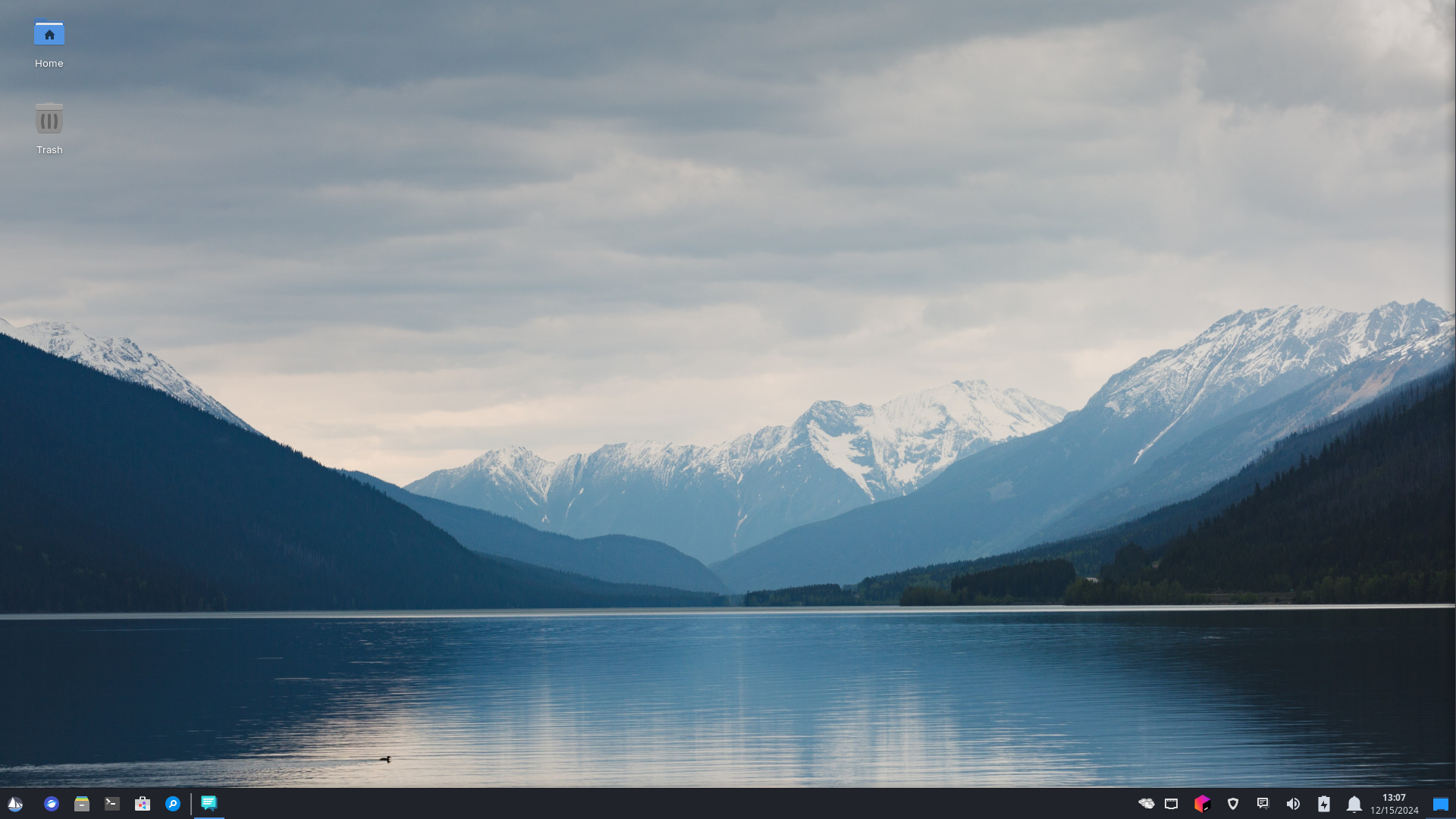 The default Solus XFCE4 experience, with a panel on the bottom, launchers and tasklist on the left, and clock and status tray on the right. The background depicts a lake with dark, white capped mountains in the background and a cloudy sky. 