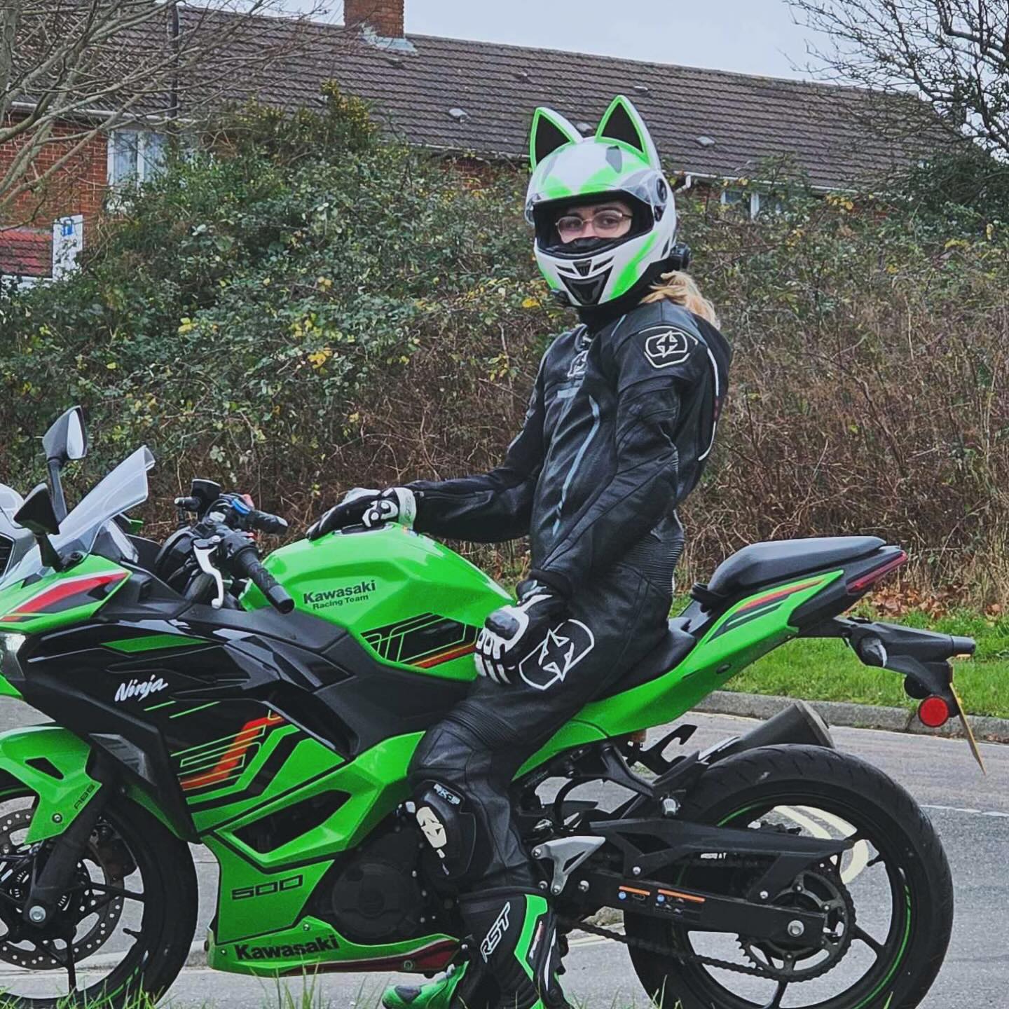 Samantha sitting on a Kawsaki Ninja 500 SE 2024 with a Black Racing Suit, Green and White Cat Eared Helmet on.