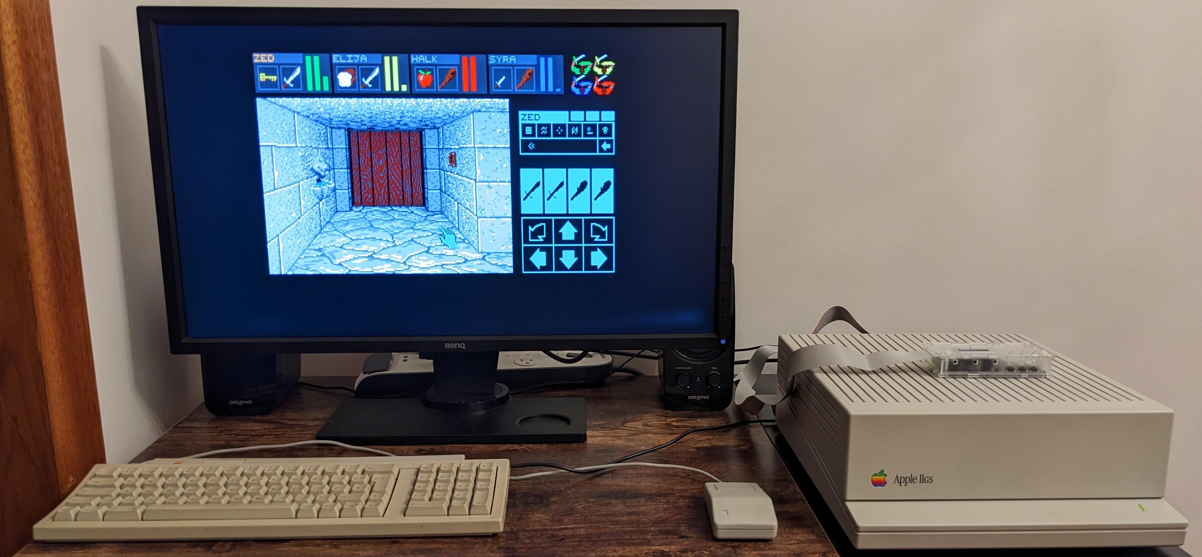 Apple IIGS on a desk attached to a Benq monitor via an unseen OSSC, with an Apple keyboard an mouse from roughly the same era, running Dungeon Master from a Floppy Emu.