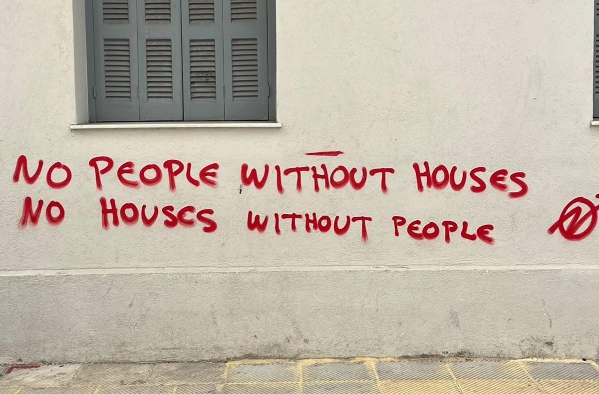 A red graffiti saying: "No people without houses, no houses without people". The symbol of squatting is drawn beside the text.