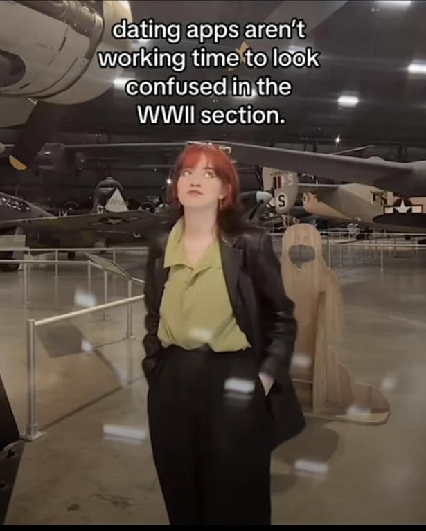 A woman in an aircraft museum with the text "dating apps aren't working, time to look confused in the WWII section"