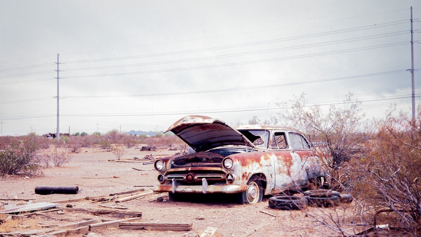 abandoned car found out in the desert near some abandoned structures