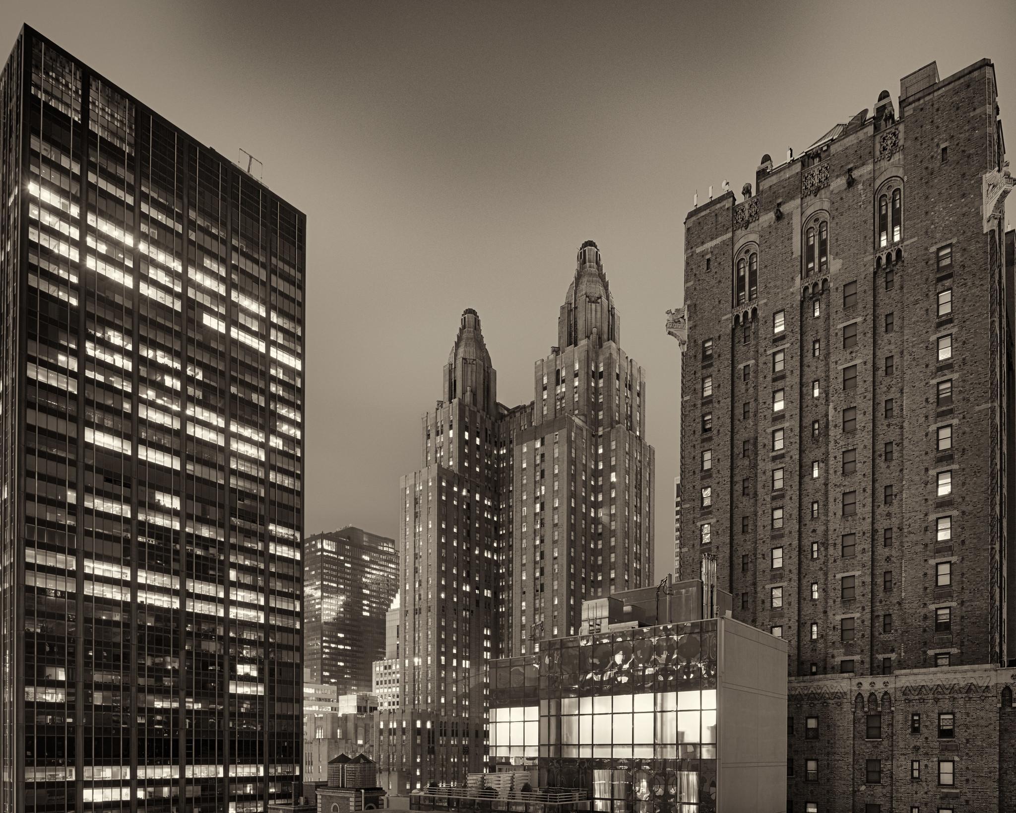 A dual-tower early 20th century skyscraper hotel building, flanked by a modern office tower at left and a large residential building at right, on a stormy night.