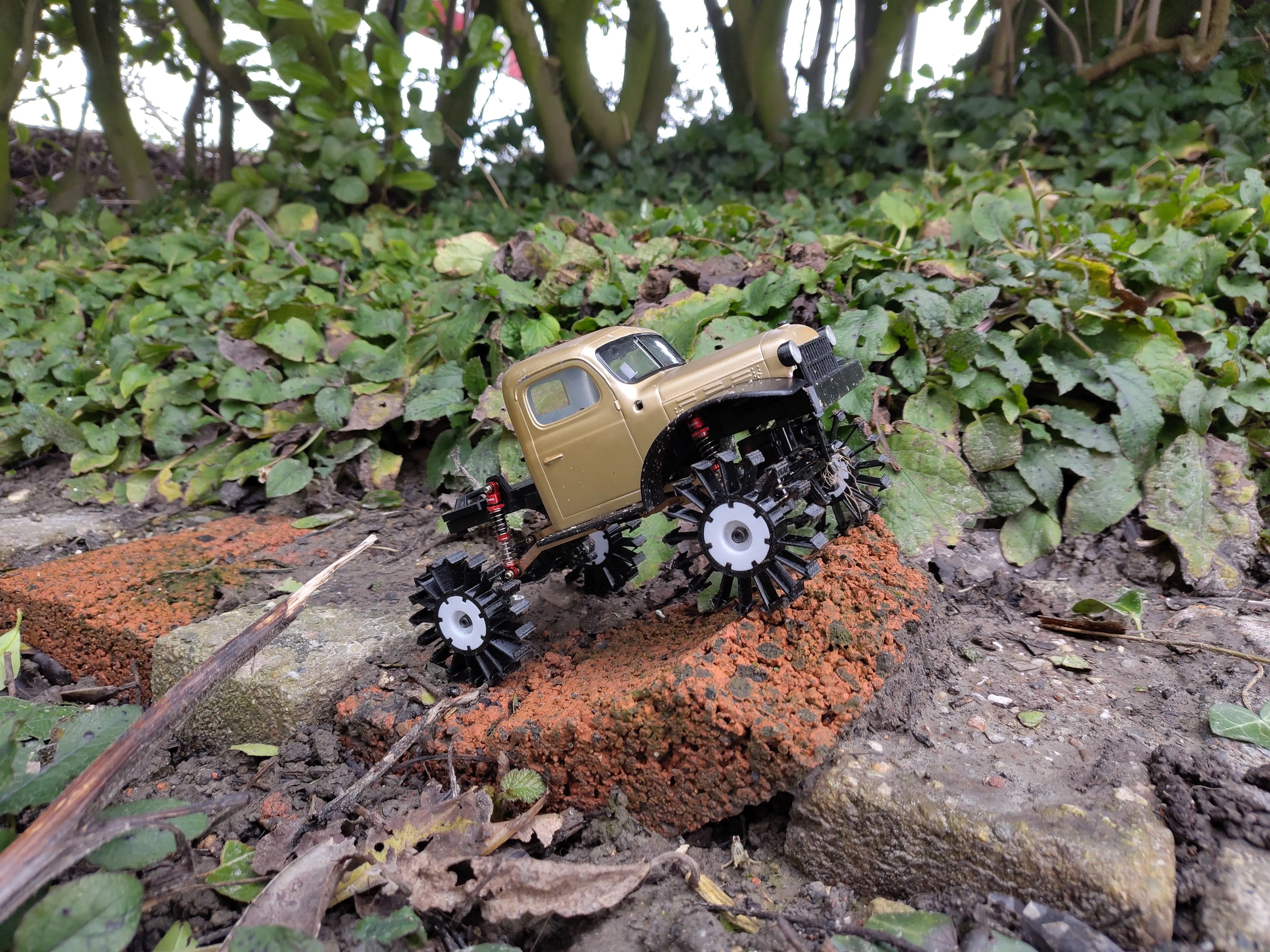 scale 24 power wagon RC car parked at a stone showing wheels with a white solid hub and outwards poiting arrows made of plastic in stead of tires